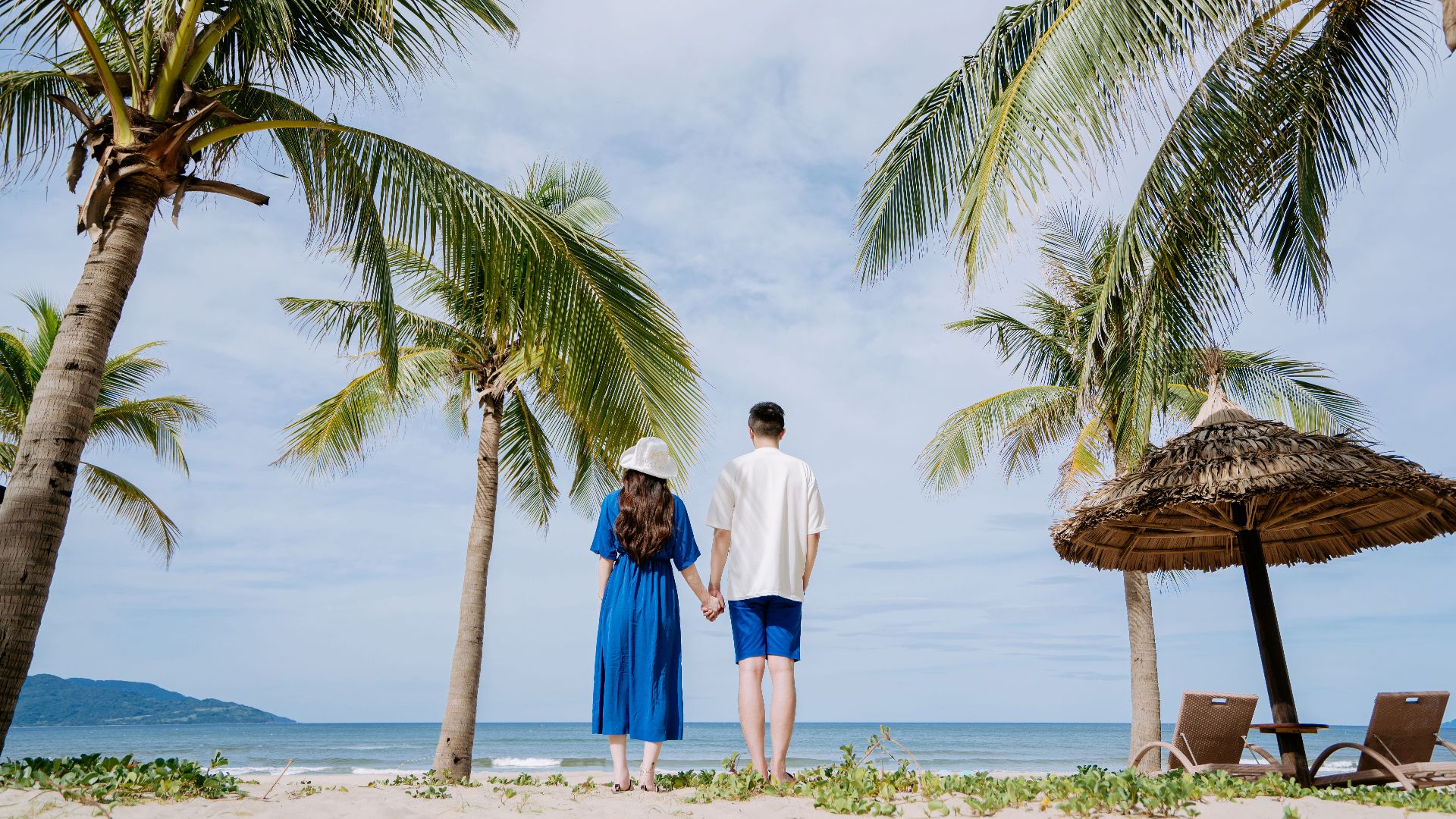 Couple holding hands on a tropical beach surrounded by palm trees, enjoying a serene vacation.