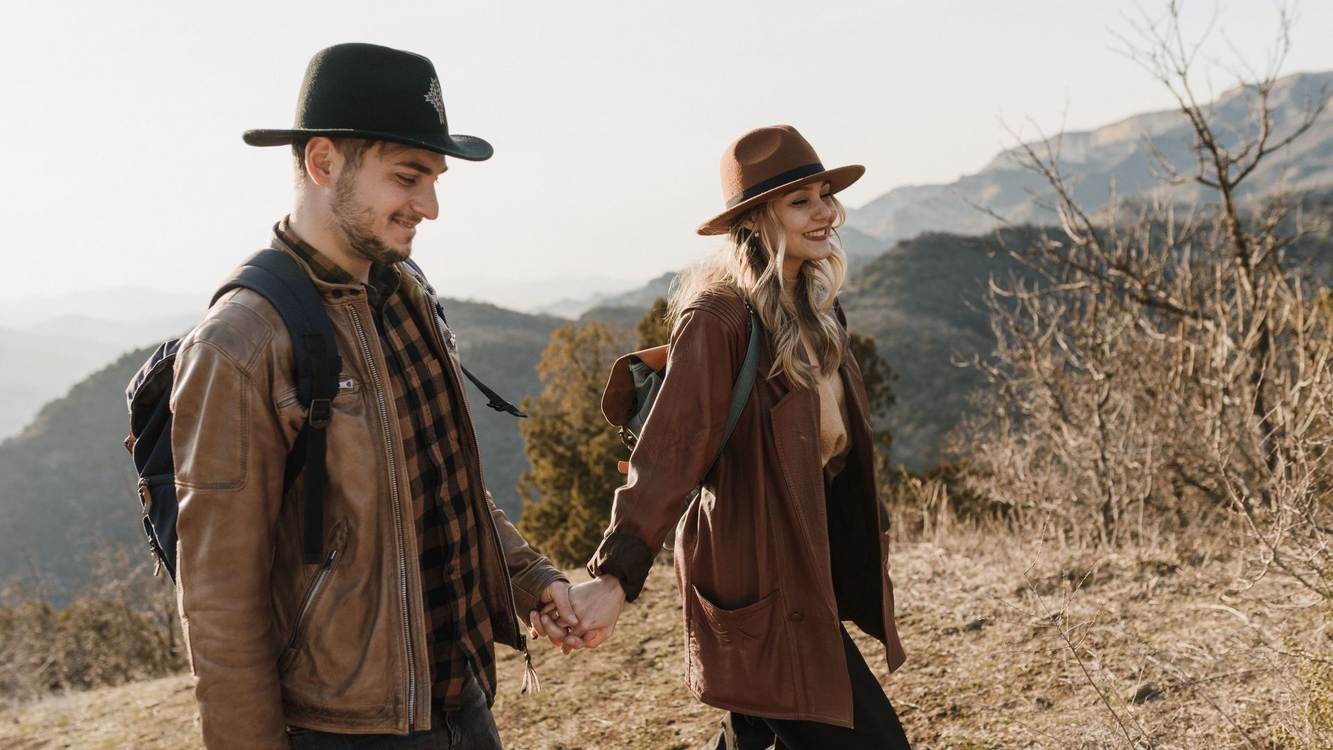 A couple enjoying a hike in a scenic mountain setting, holding hands and smiling.