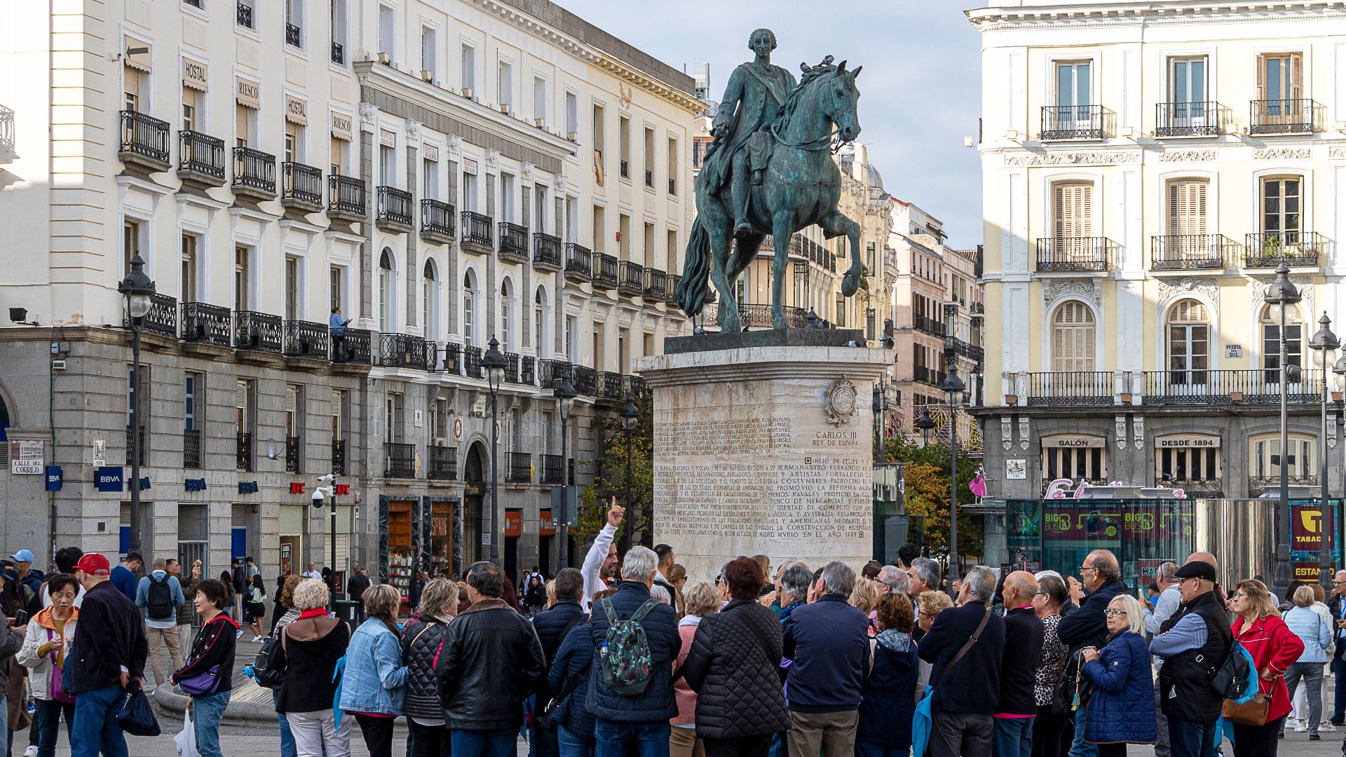 Tourists gather around the equestrian statue in Madrid's Puerta del Sol. Vibrant urban scene.