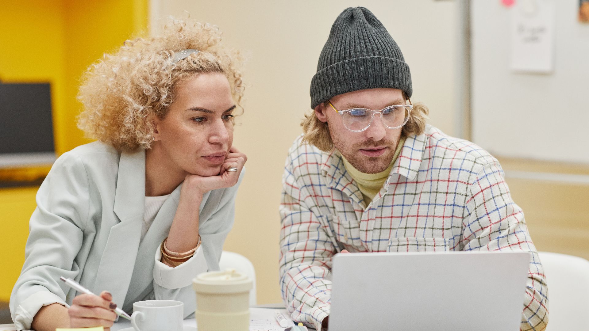 Two professionals discussing ideas at a desk with a laptop and notes in an office setting.