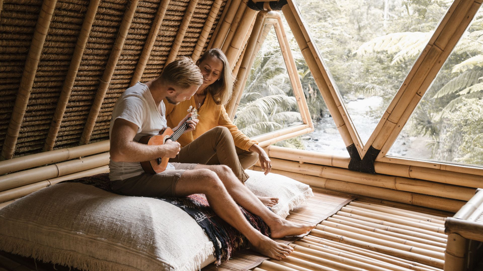 Couple enjoying music and relaxation in a bamboo house setting.