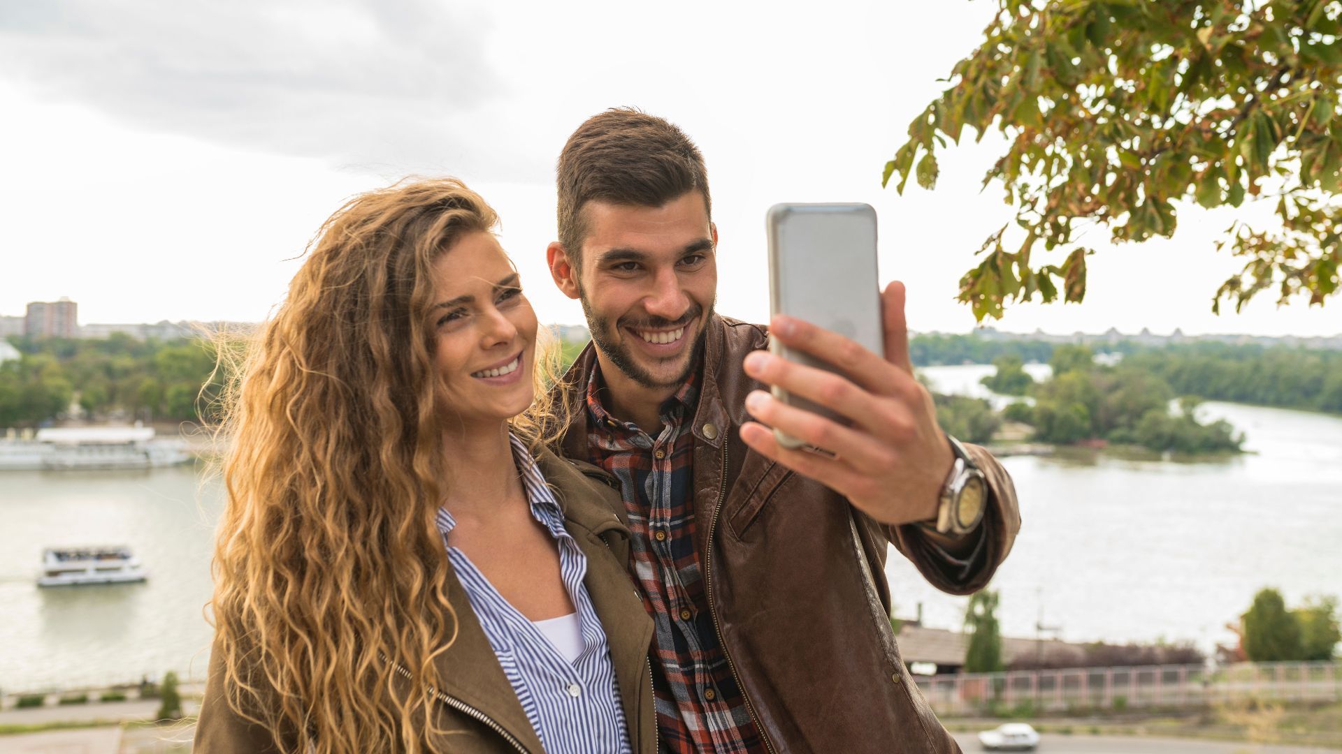 A joyful couple taking a selfie near a scenic river view, capturing special moments together.