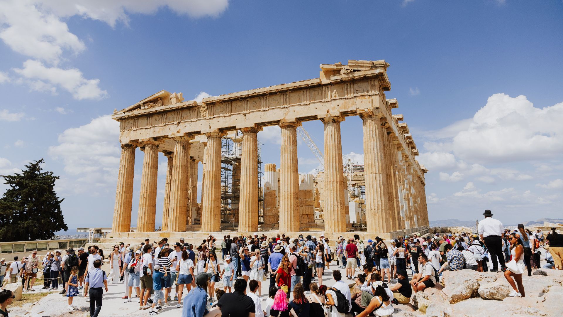Tourists gather at the historic Parthenon in Athens under a sunny sky.