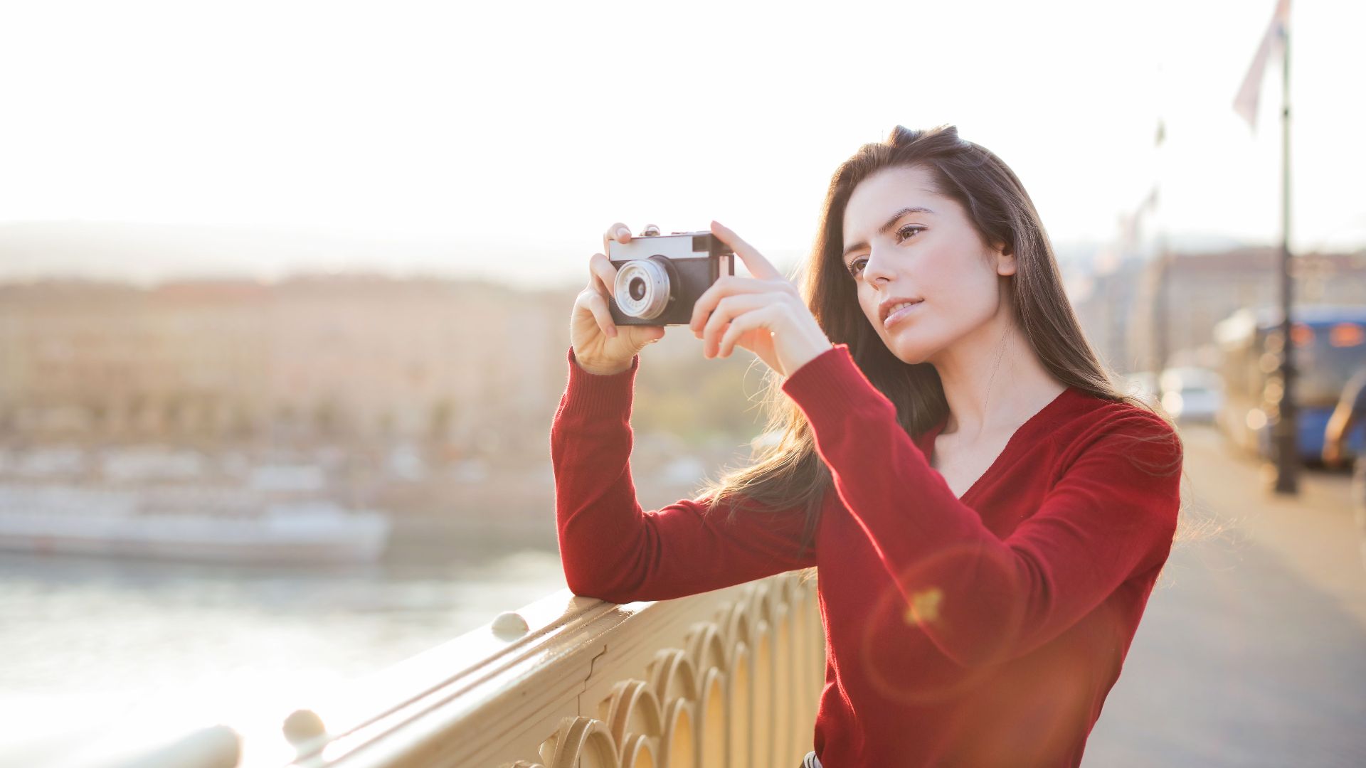 A woman in a red sweater takes a photo on a bridge during sunset, showcasing photography passion.