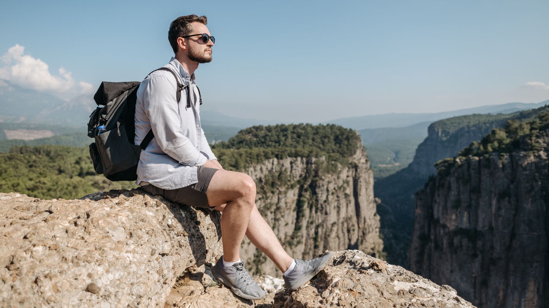 A man sits on a rock ledge overlooking a canyon, enjoying the tranquil outdoor scenery.