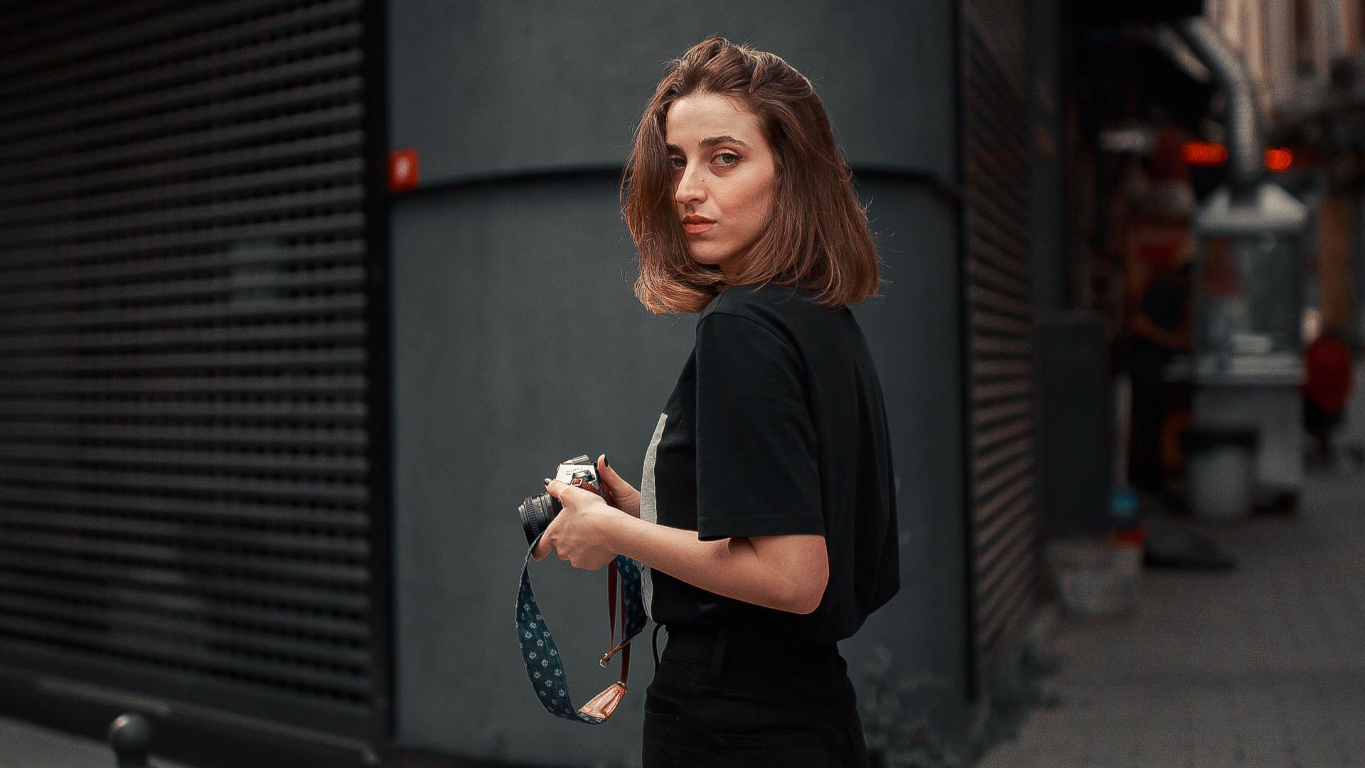 Stylish woman in black clothes looks at the camera while standing on a city sidewalk.