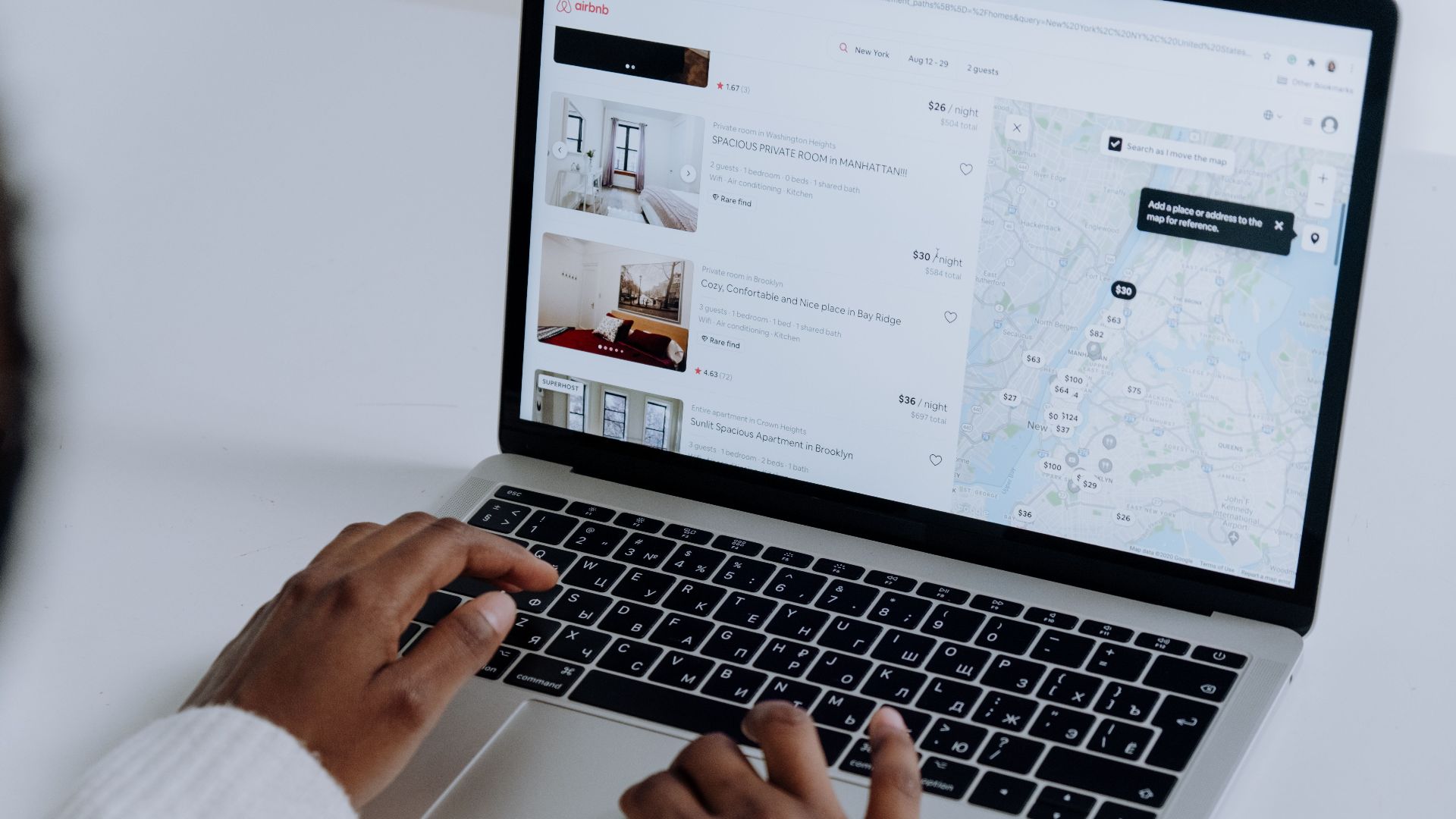 Hands typing on laptop searching Airbnb for accommodation options with map view.