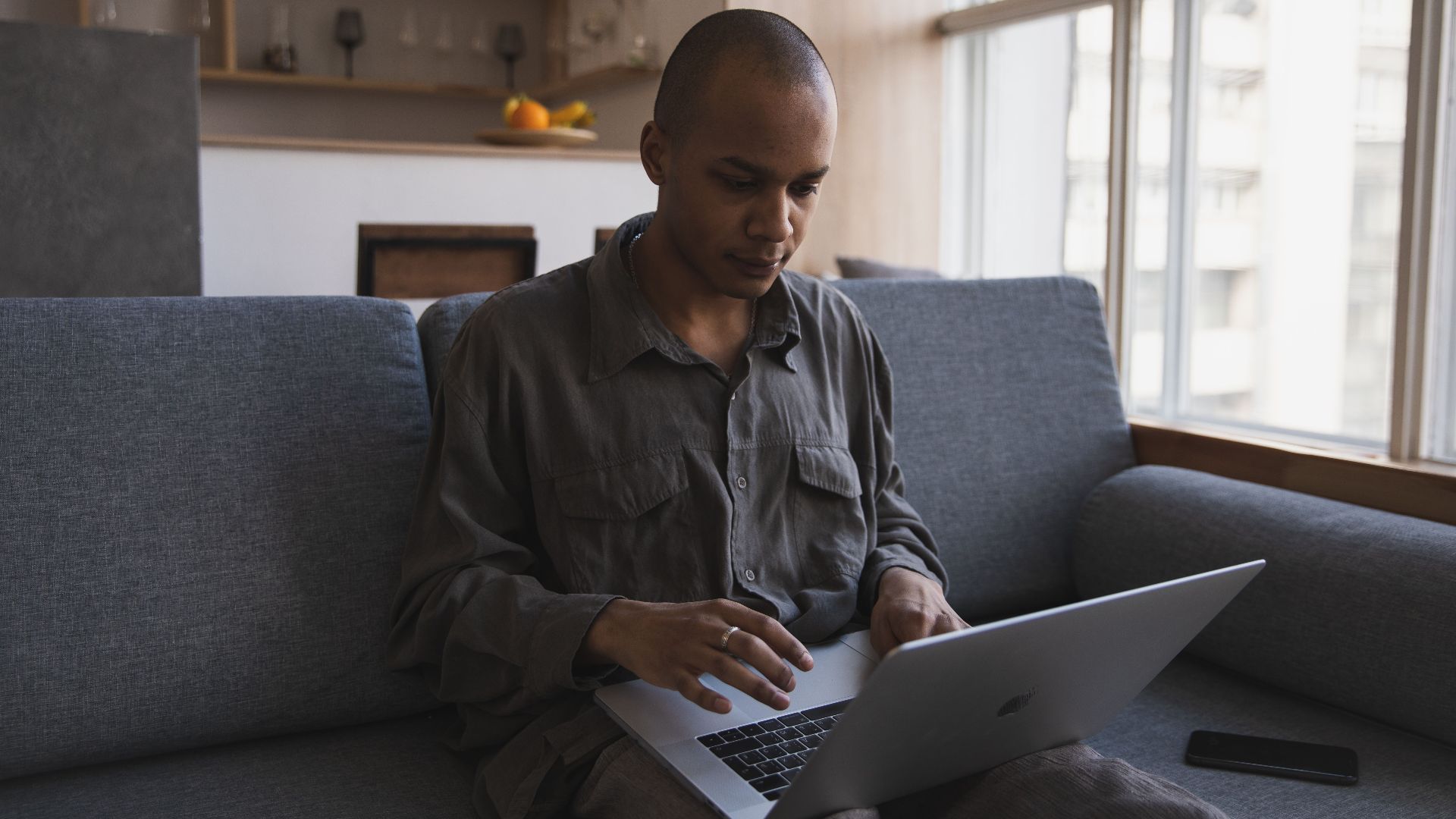 Man working intently on a laptop while sitting on a sofa in a modern room.