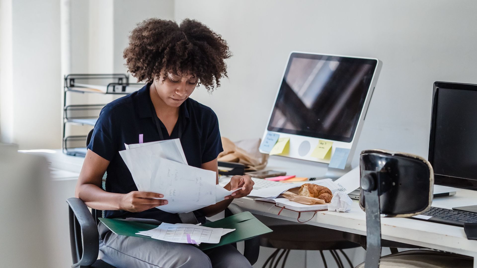 Young businesswoman multitasks with documents and laptop in a modern office setting.