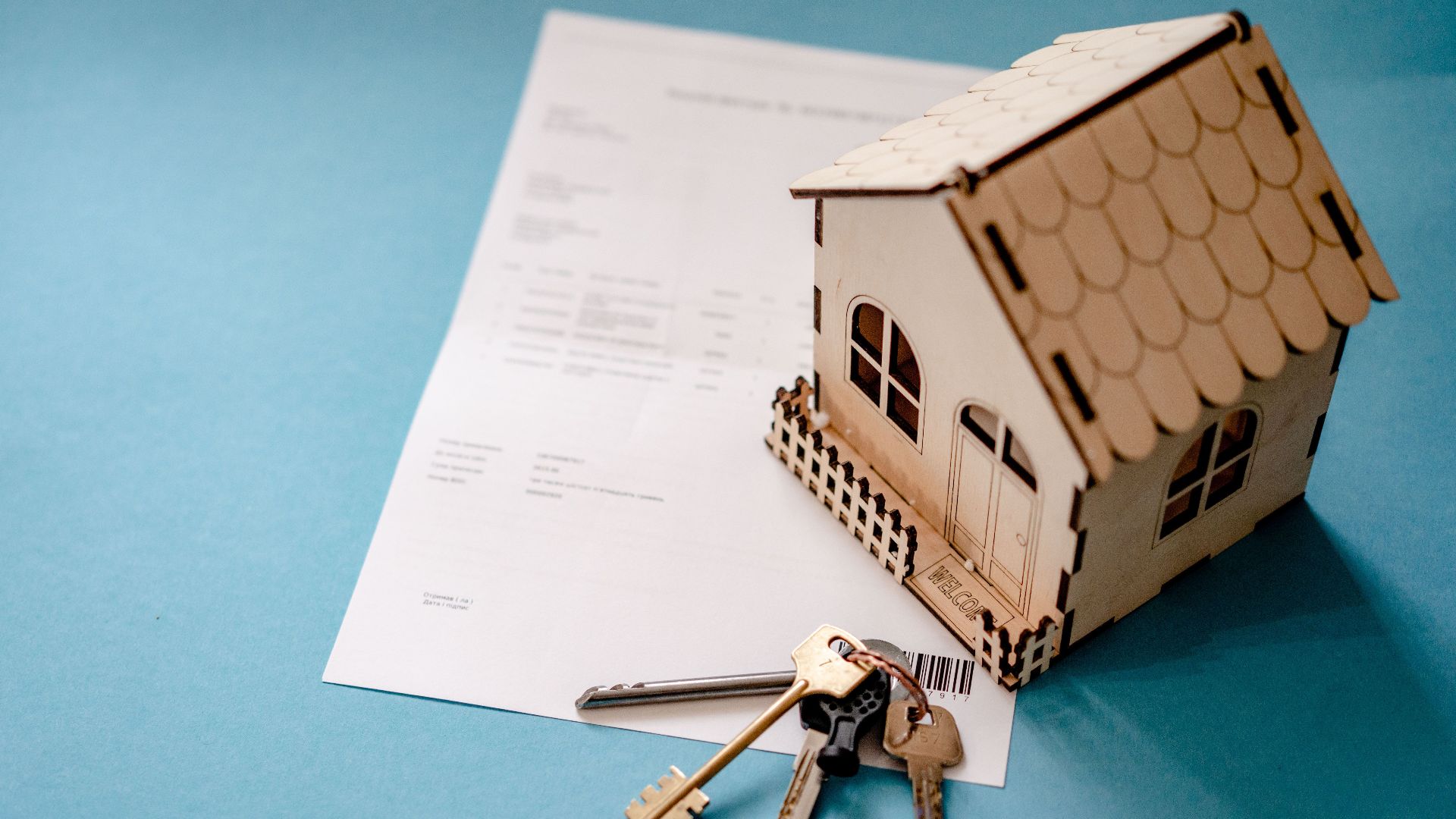 Miniature wooden house with keys and contract symbolizing real estate transactions.