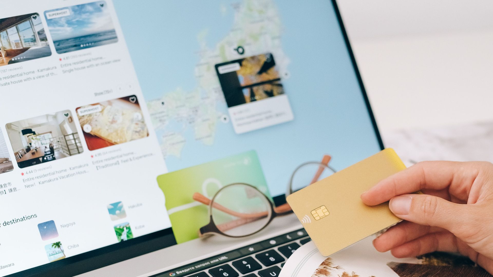 Hands holding credit card over laptop and magazine for online shopping and travel planning.