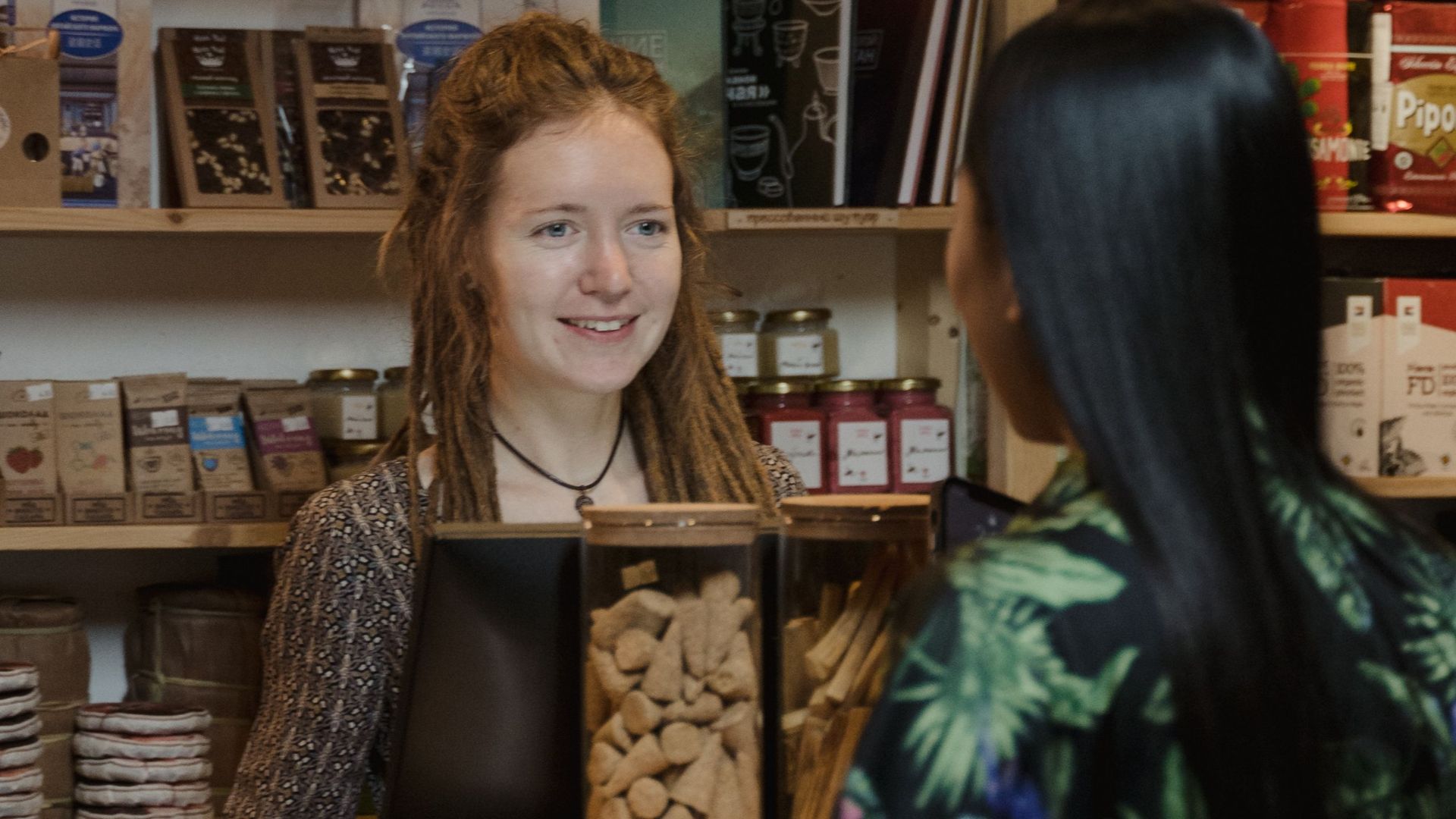 A customer exchanges smiles with a shopkeeper in a warm, inviting store environment.