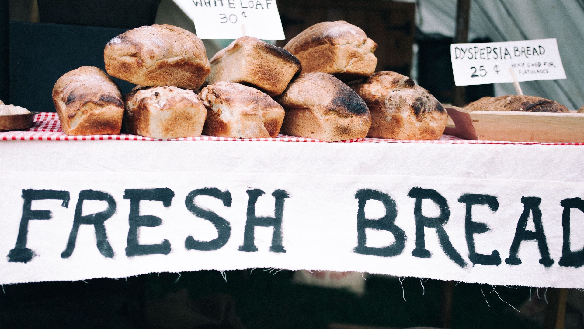 Loaves of fresh bread on display at a market stall with hand-painted signs.