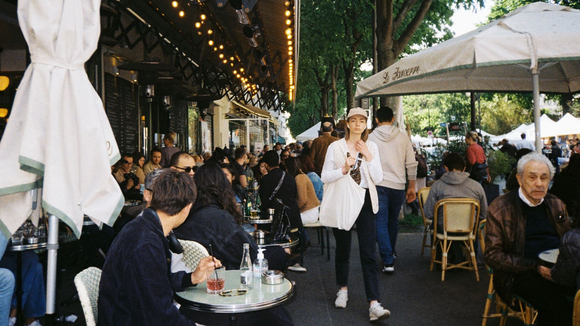 Cozy outdoor city café bustling with people enjoying leisure time under umbrellas and trees.
