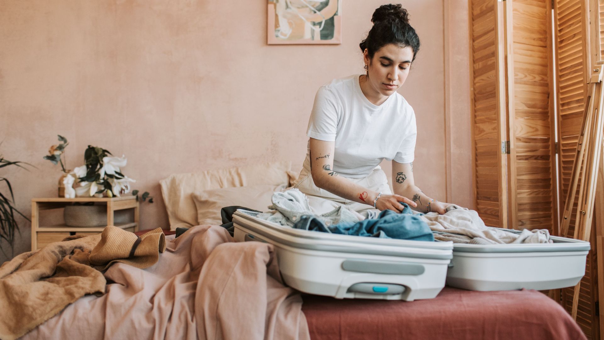 A woman packing her suitcase with clothes in a stylish and cozy bedroom setting.