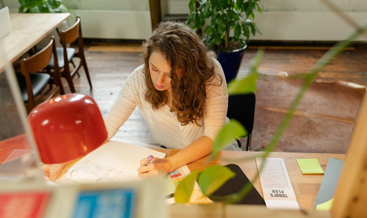A woman with brown hair working intently at a desk, indoors in an office environment