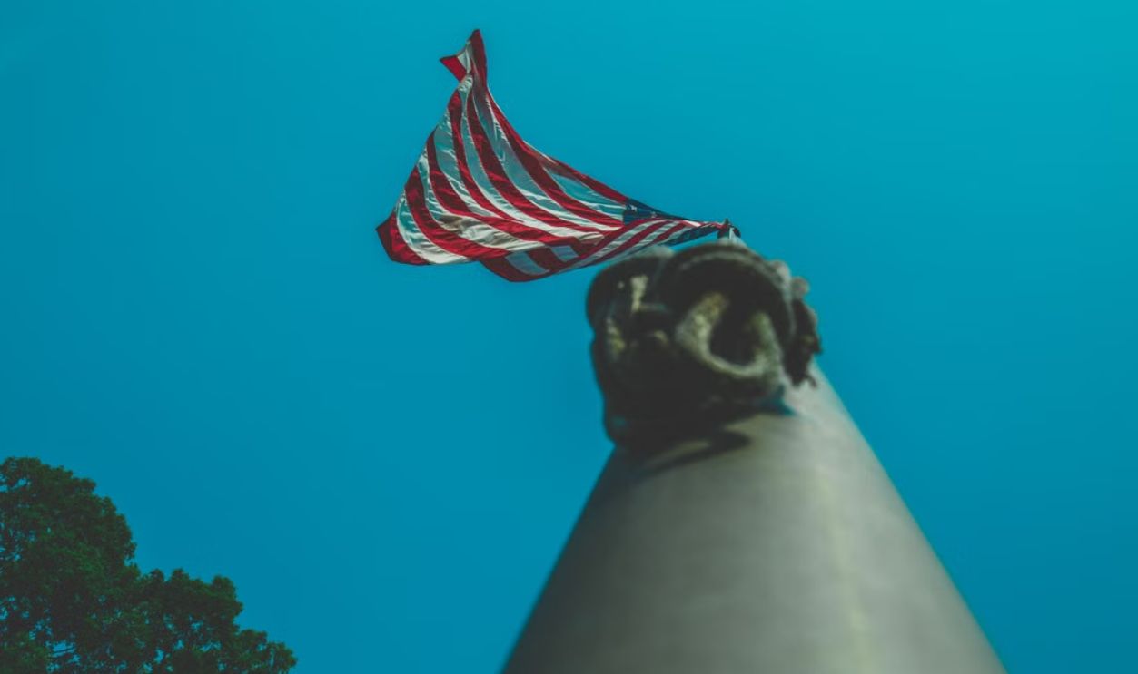 Upward perspective of the American flag on a flagpole against a clear blue sky