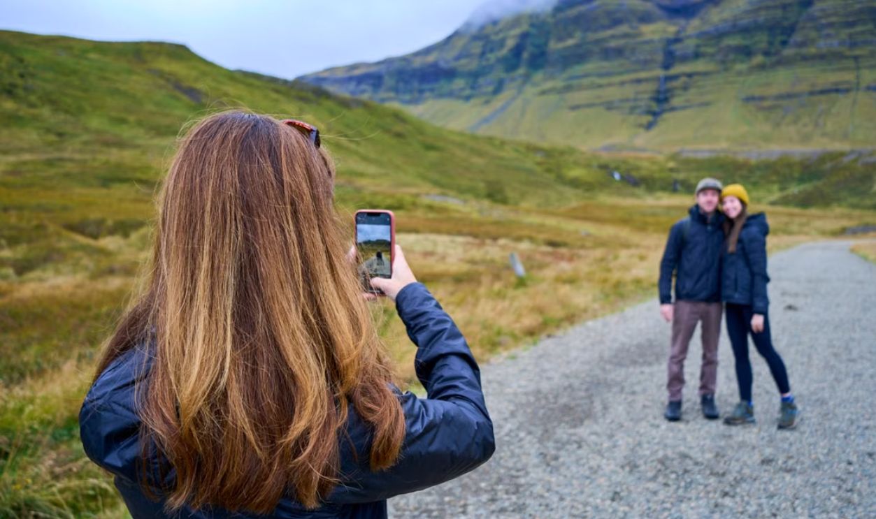 Woman taking a picture of a couple in a picturesque mountain landscape, capturing memories of their adventure