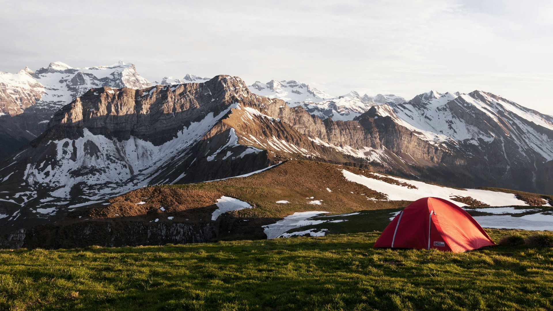 red tent on grass field beside ice capped mountain nature photography