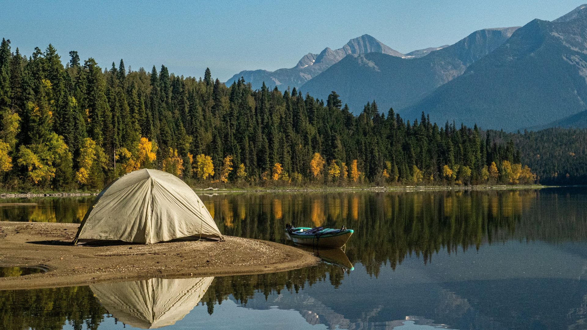 white tent on lake near green trees and mountain under blue sky during daytime