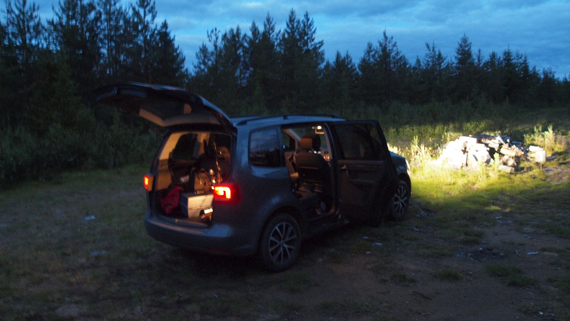 A Volkswagen Touran car in the middle of the wilderness in Tulppio, Savukoski, northern Lapland, Finland, in the middle of the night. The car is shining its headlights directly onto a pile of wooden logs. The car had been previously used to travel to a fi
