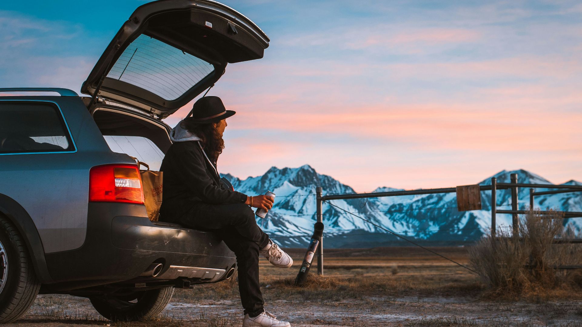 man sitting on car's tail looking at ranch