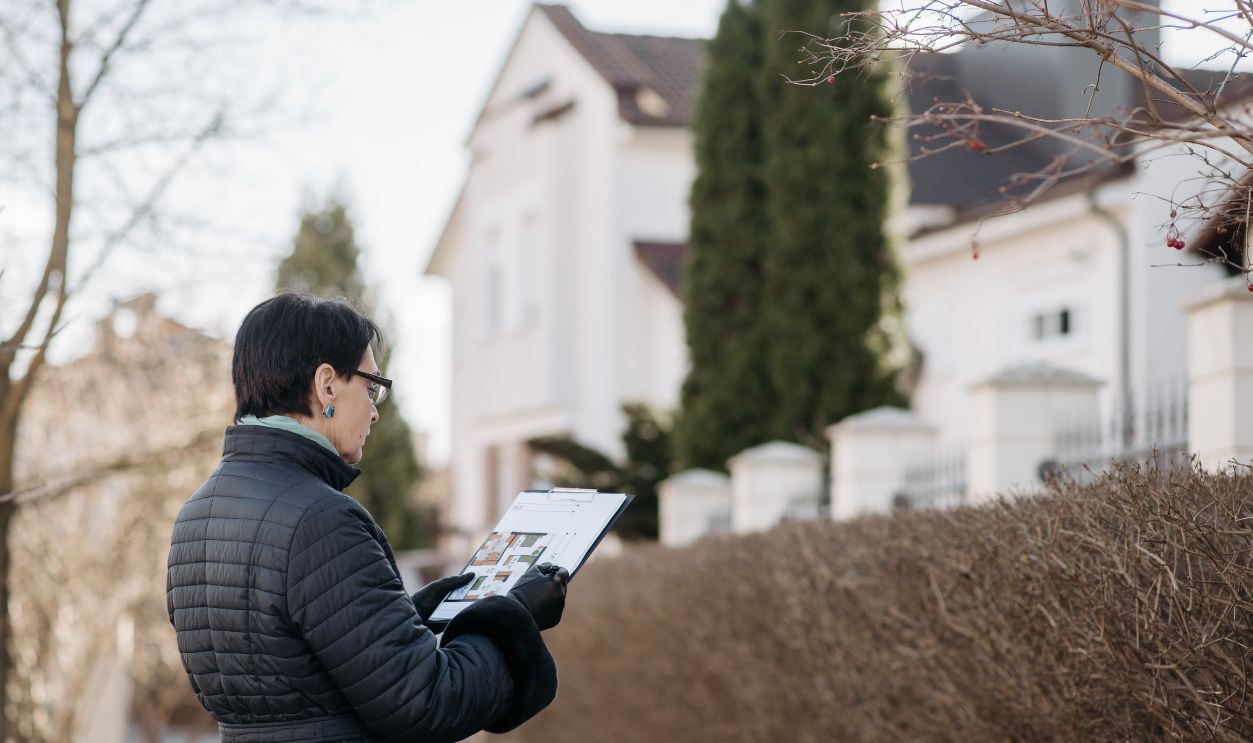 Realtor assessing house with clipboard during winter season outdoors. Ideal image for real estate content
