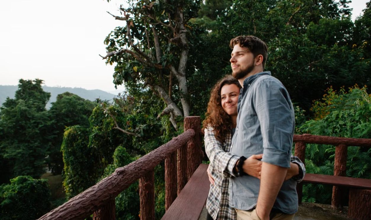 A couple embraces on a scenic deck surrounded by lush forest foliage, showcasing love and nature
