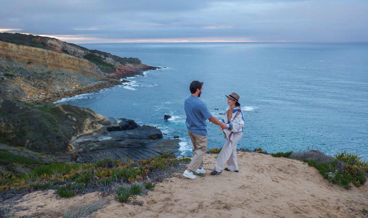 A couple enjoying a romantic moment on a cliff overlooking the ocean at sunset.