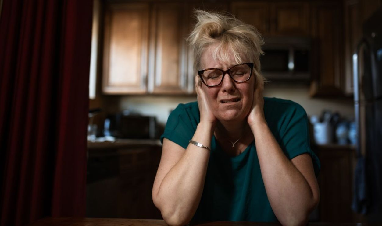 An adult woman in distress sitting at a table indoors, conveying emotional struggle