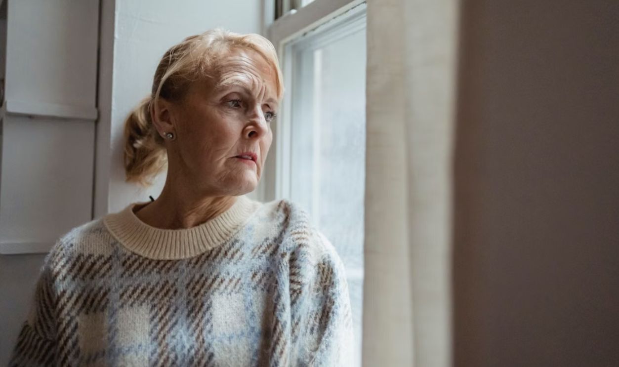 A senior woman in deep thought gazing out a window indoors