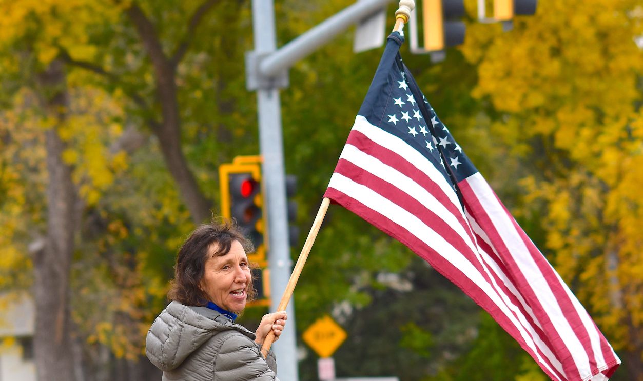 A smiling protester waving an American flag in a park during a peaceful demonstration