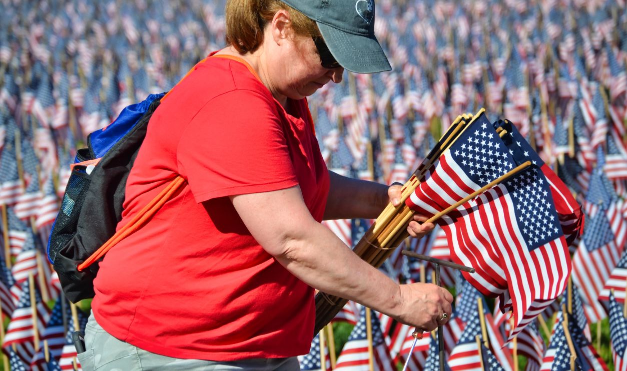A woman in Boston arranges American flags as part of a memorial display on a sunny day