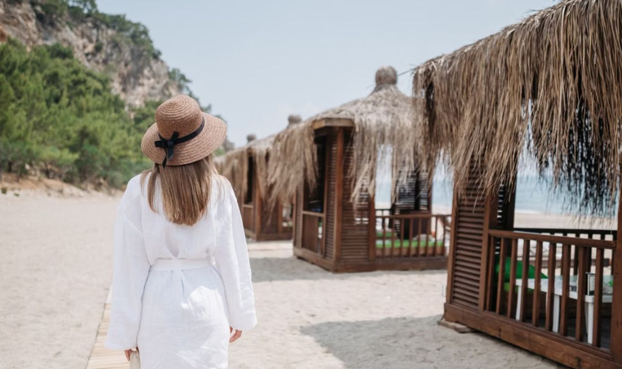 A woman in a sunhat walks along beach huts on a sunny day, enjoying a vacation atmosphere