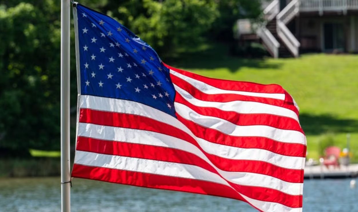 Vibrant American flag waving by a picturesque lake with a house backdrop, capturing summer spirit
