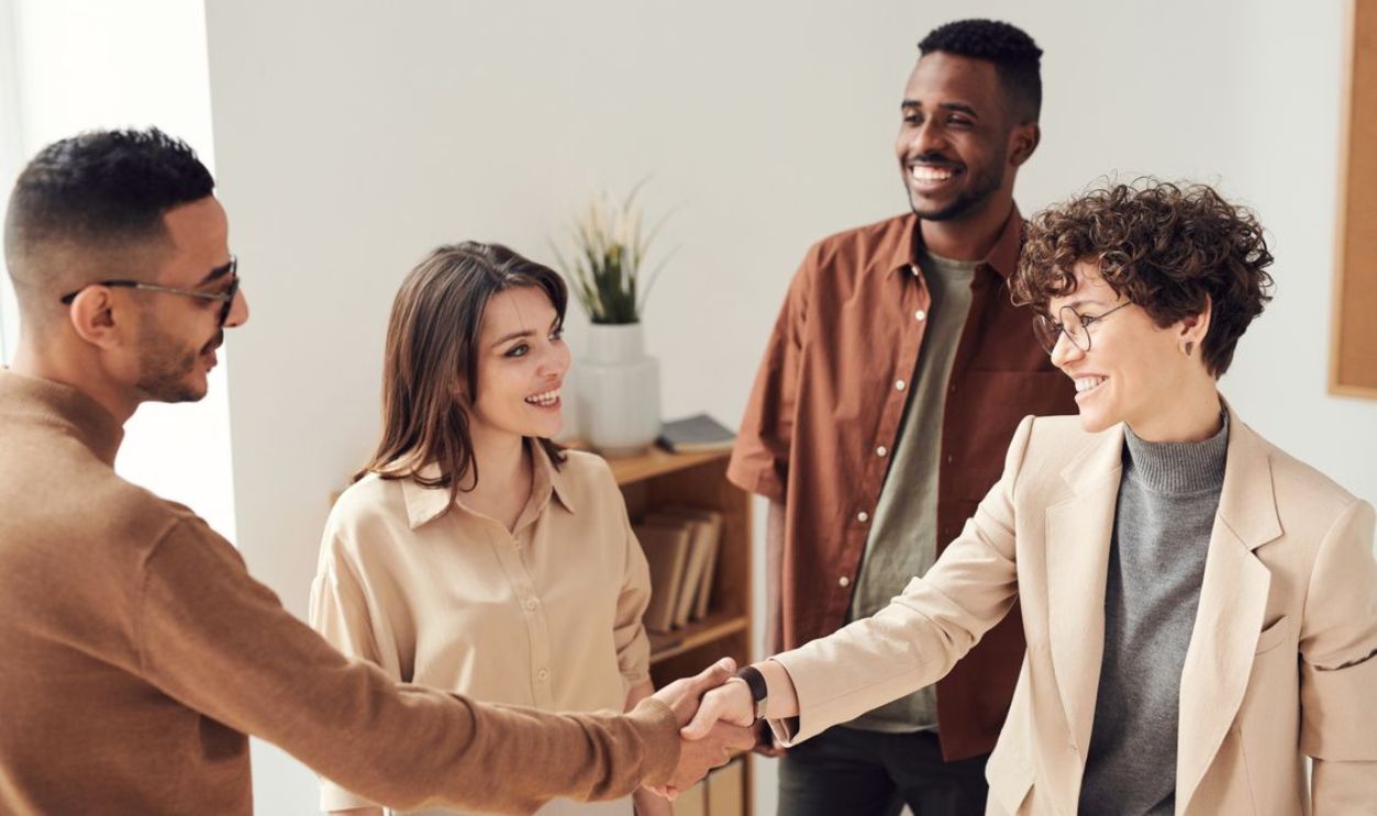 Four colleagues smiling and shaking hands in a bright office setting.