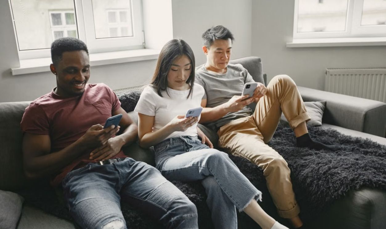 A group of diverse friends lounging on a sofa, each using a smartphone.