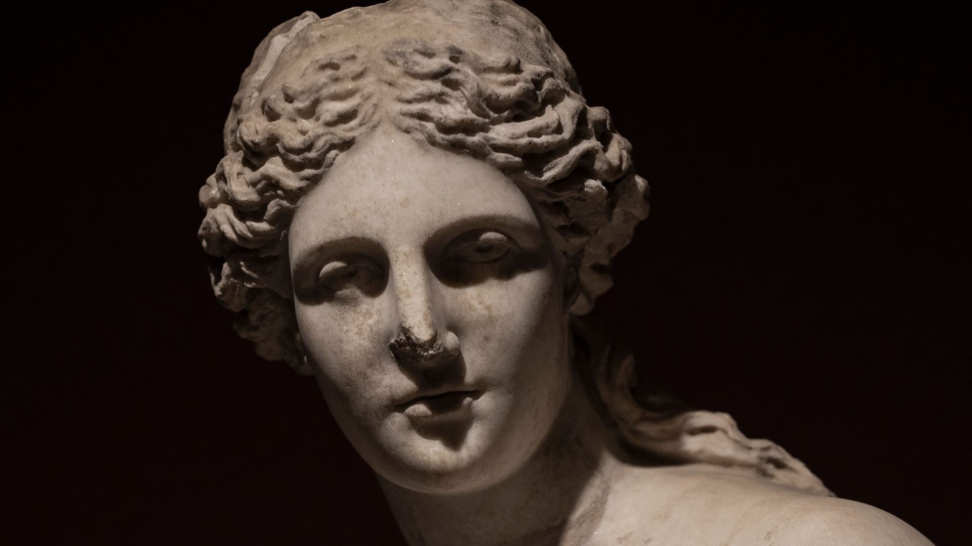Detailed photograph of a marble statue of Aphrodite with a dark background.