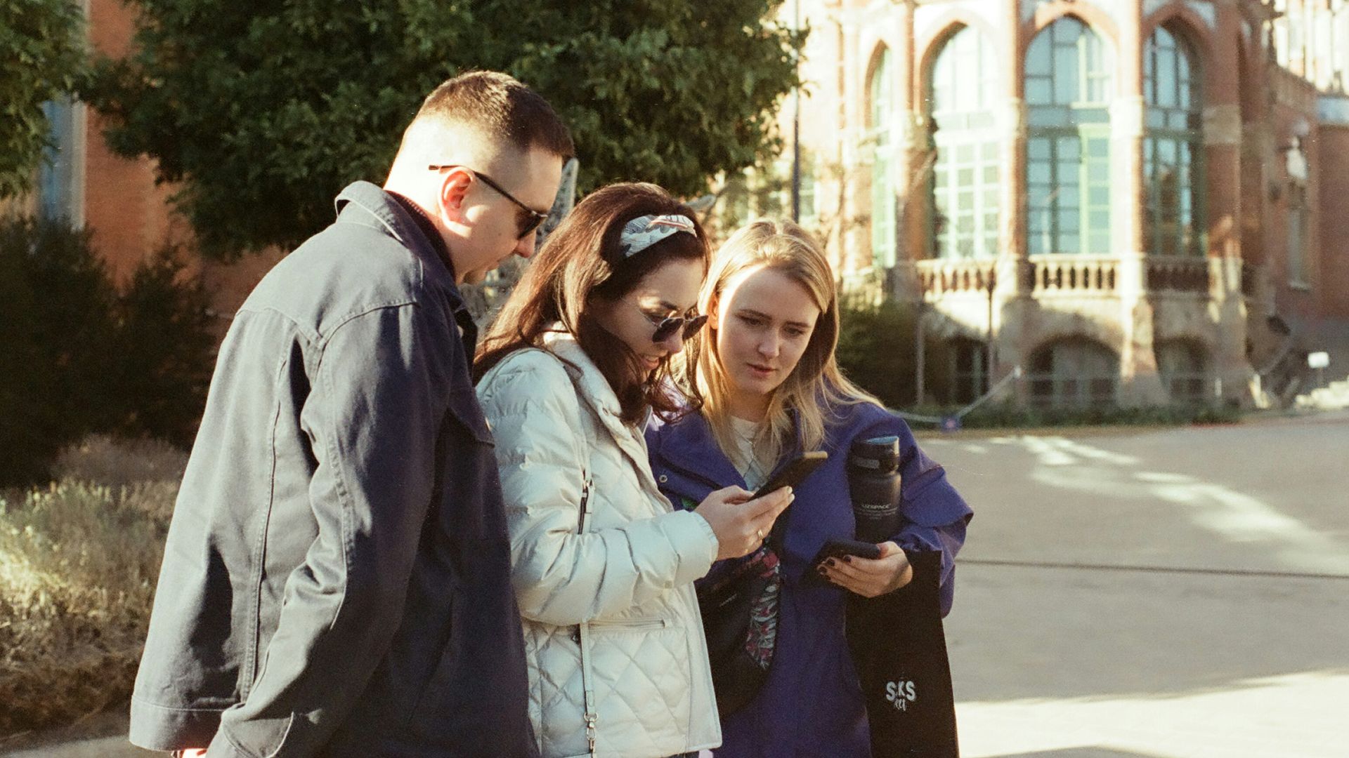 a group of people standing on a sidewalk looking at a cell phone
