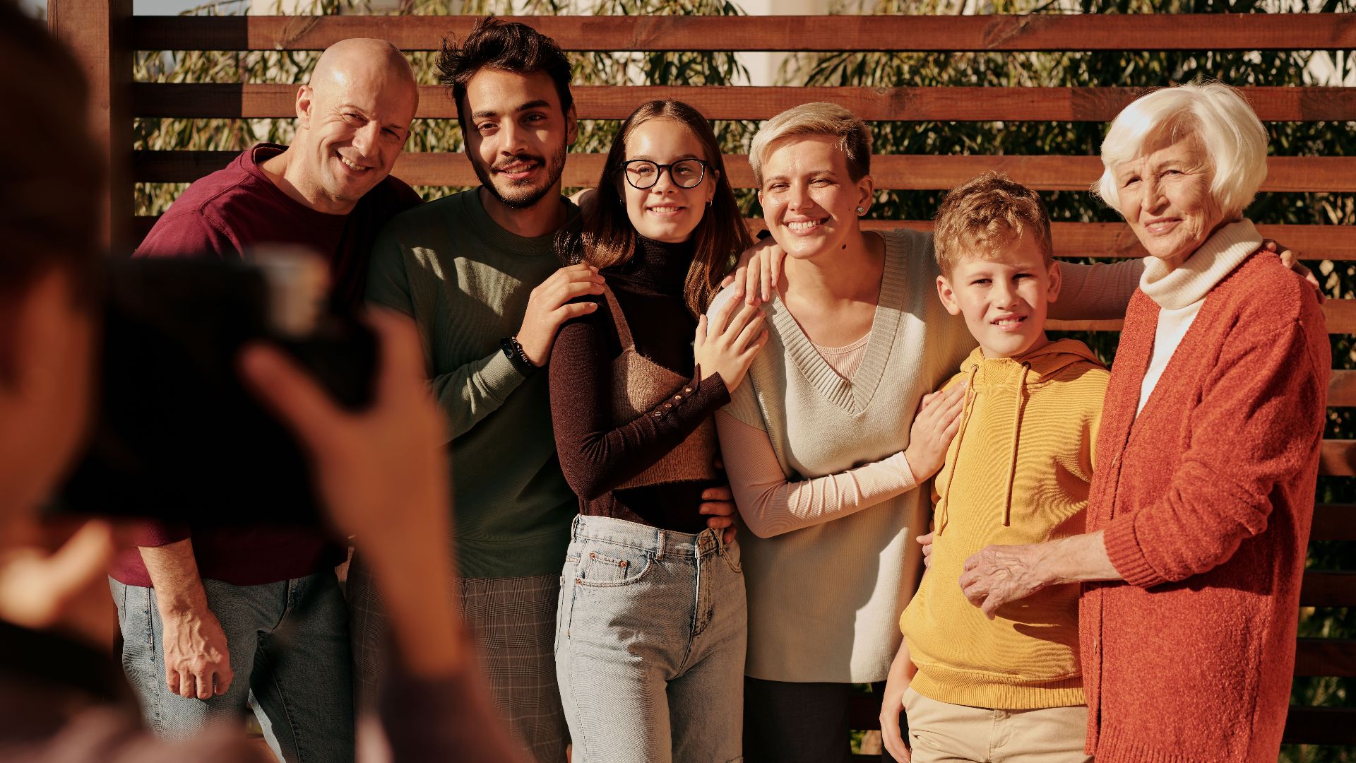 A joyful family portrait featuring multiple generations smiling outdoors in daylight.