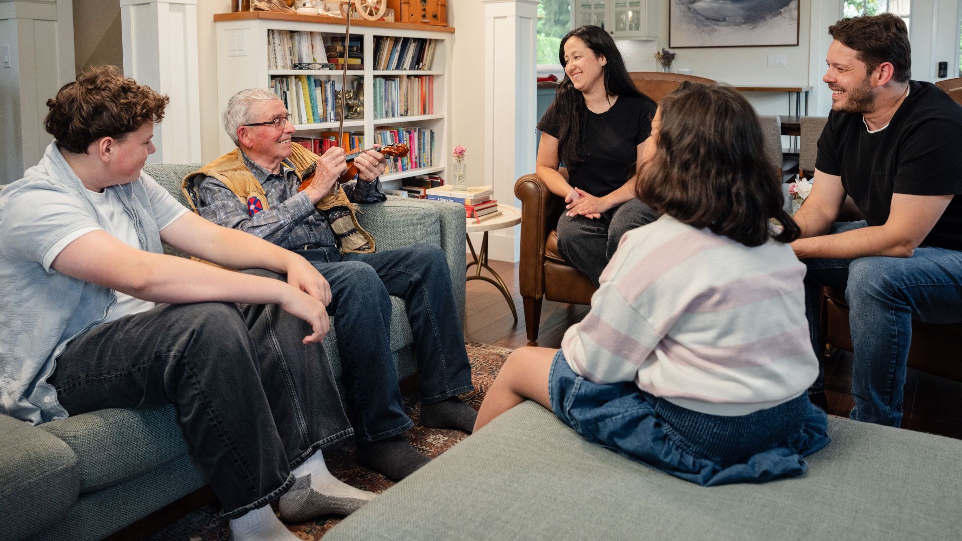 A joyful multigenerational family gathering in a cozy living room, sharing stories and playing a violin.