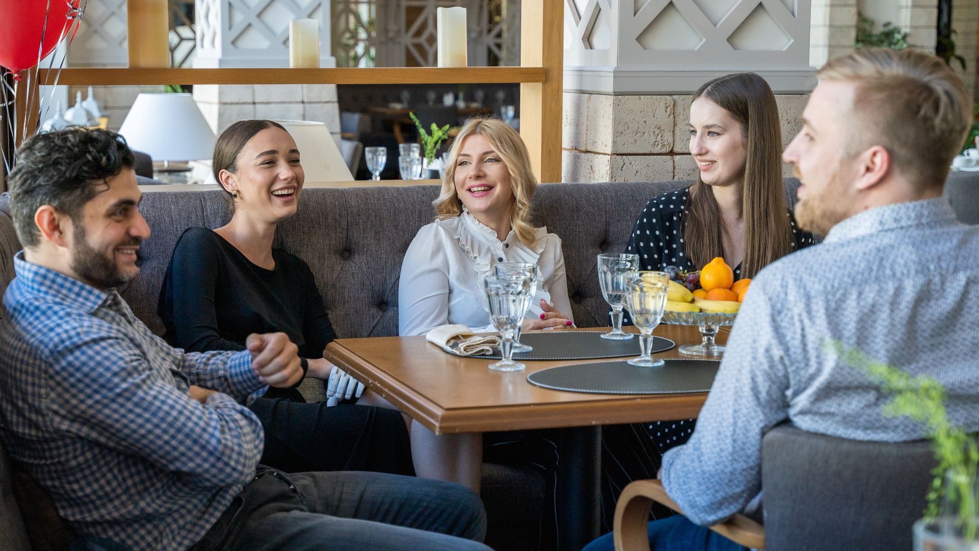 Five adults having a joyful conversation in a cozy restaurant setting indoors.