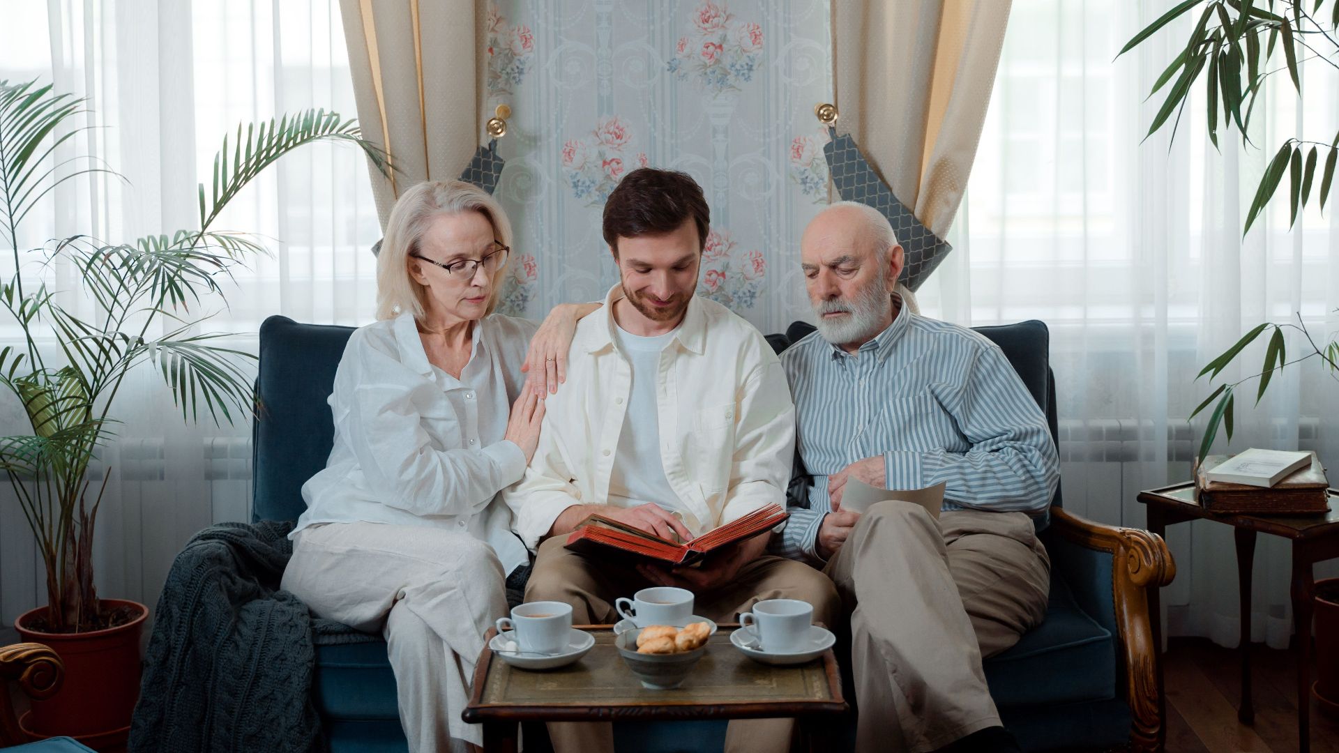 Elderly couple with son enjoying a photo album at home, sharing memories.