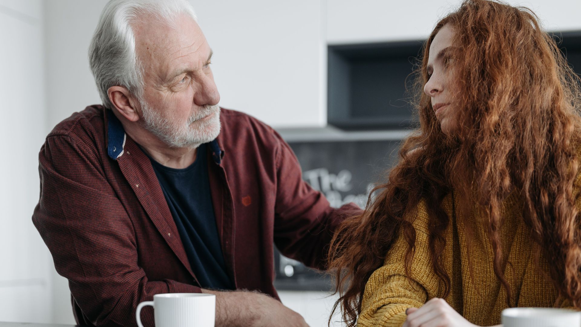 A touching moment between a grandfather and granddaughter sharing emotions indoors over coffee.