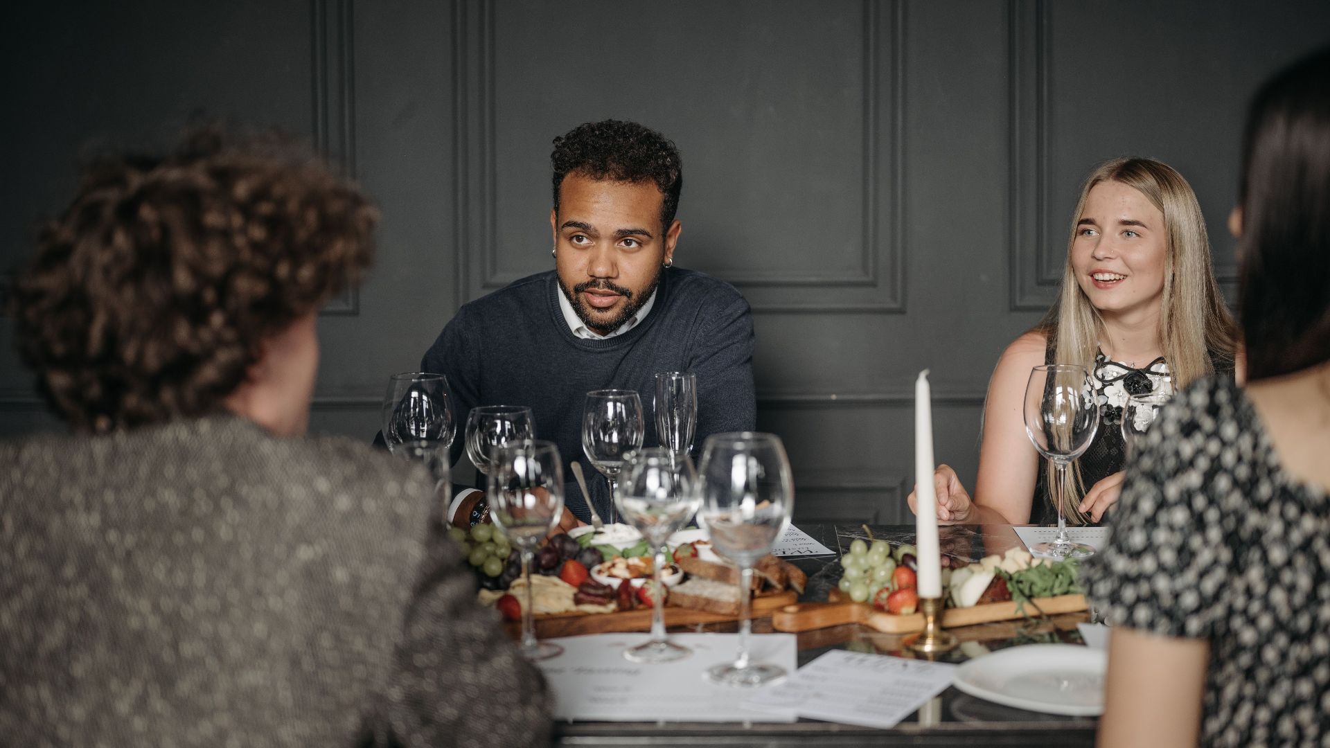 Group of friends having a conversation at a dining table set with food and drinks indoors.