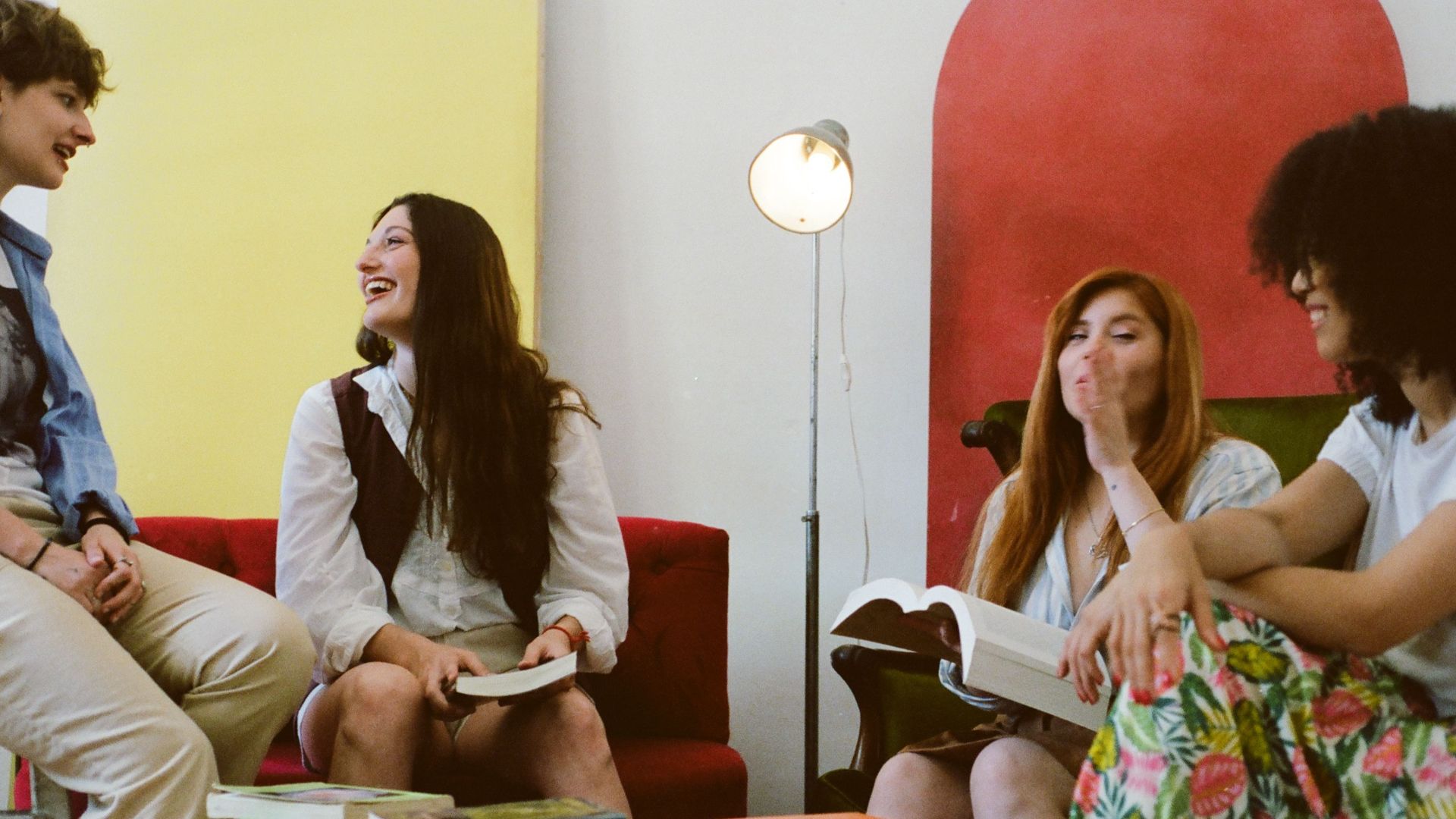 Four friends laughing and reading books in a cozy indoor setting with colorful decor.