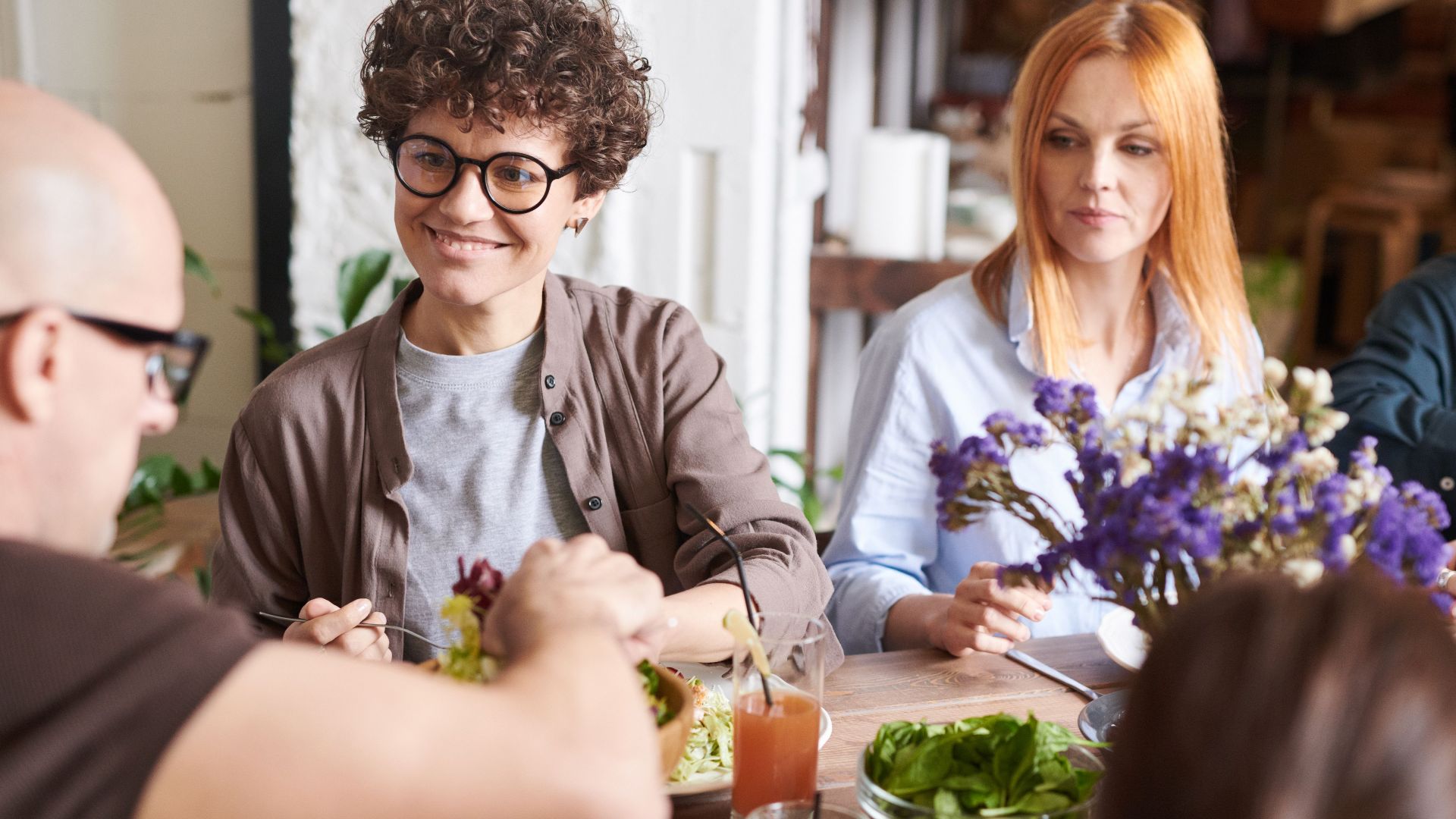 A diverse group of friends dining together at a cozy indoor setting, sharing and enjoying a meal.