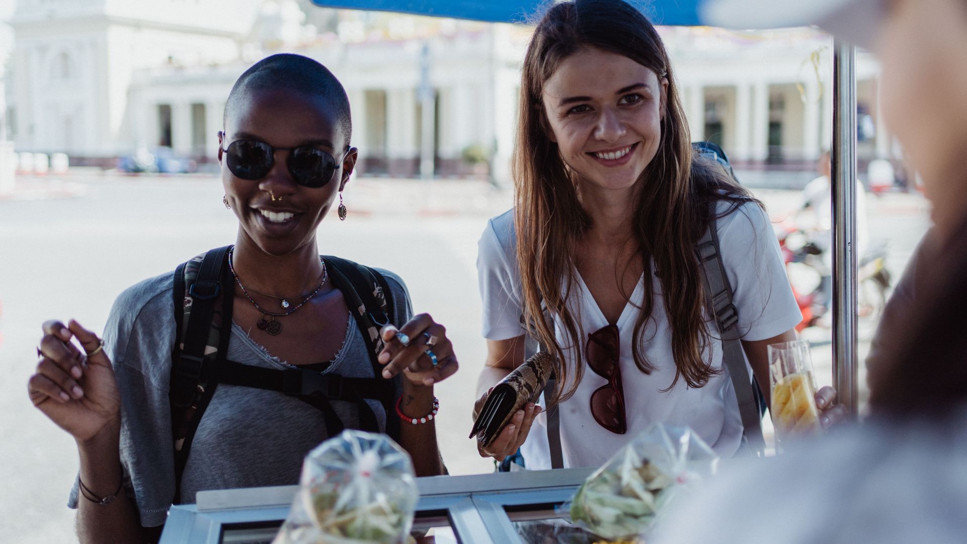 Two women enjoying street food at an outdoor market, exuding joy and travel spirit.
