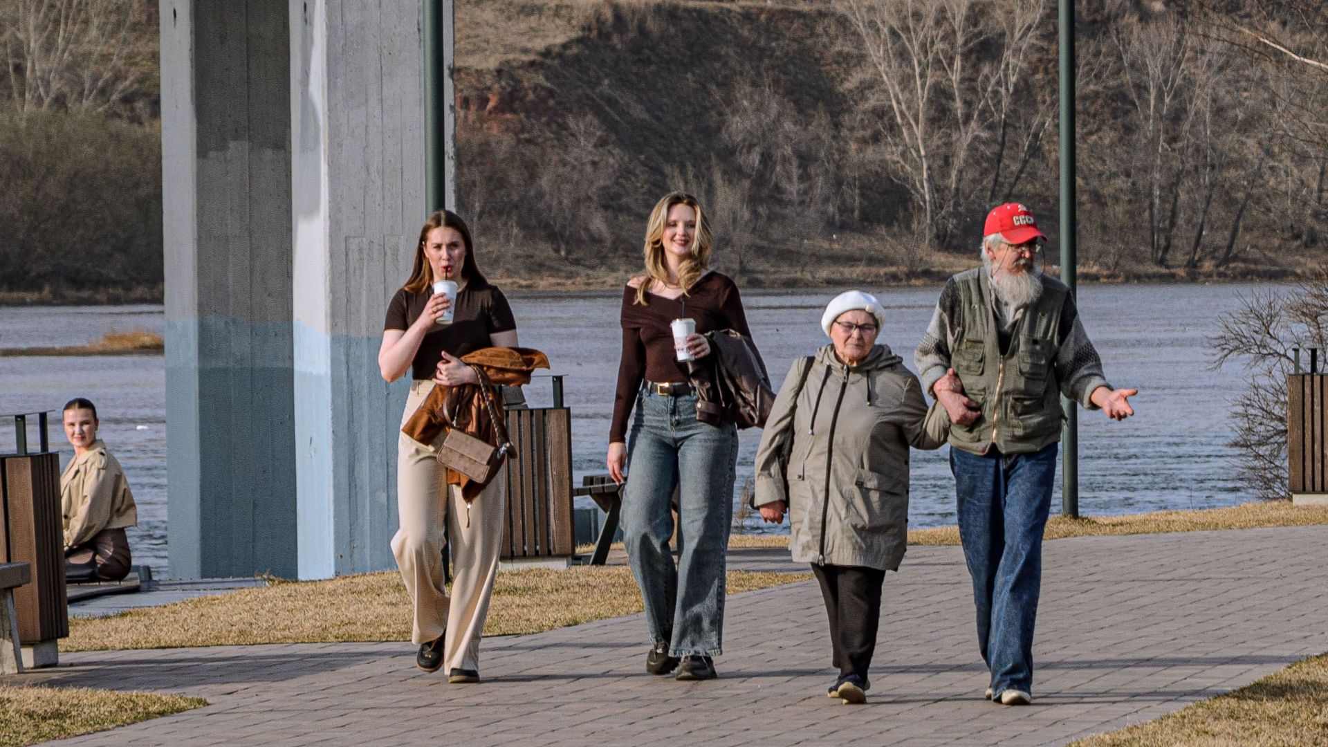 A multigenerational group enjoys a sunny walk by the riverside in springtime.