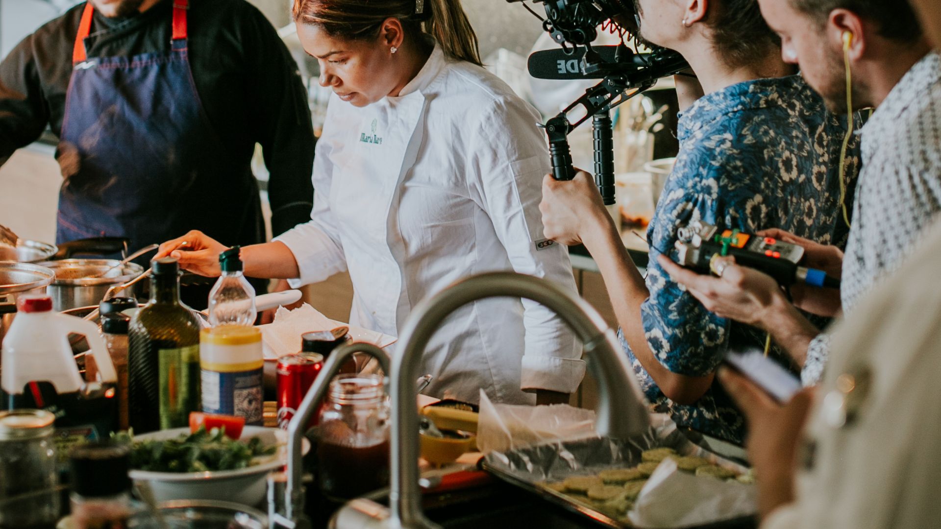 Chefs are filmed cooking in a modern kitchen, showcasing culinary skills for a show.
